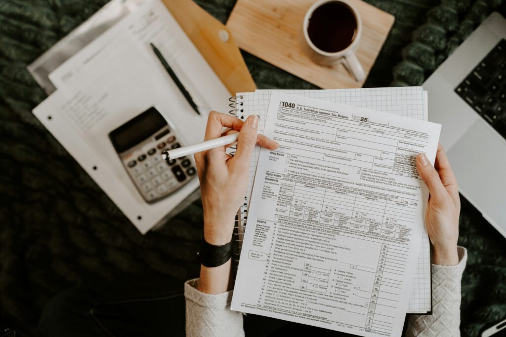Person filling out a tax form with a pen beside a calculator and coffee on a desk