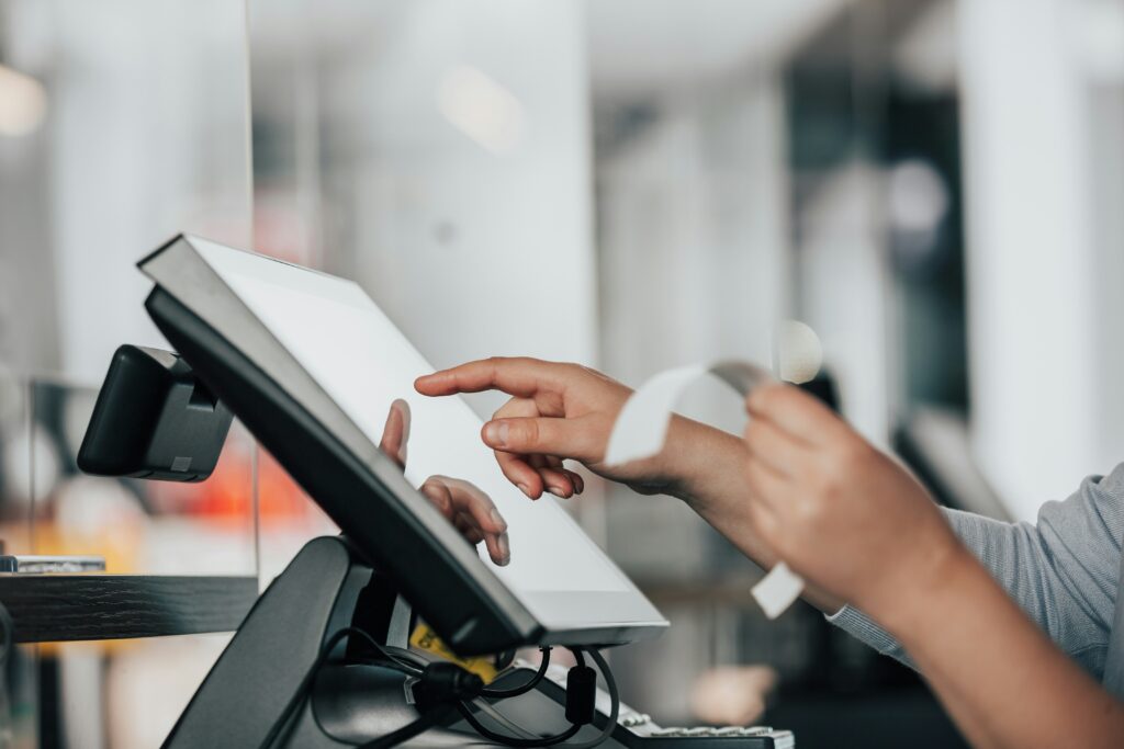 Person using a touchscreen POS system at a retail checkout counter while holding a receipt